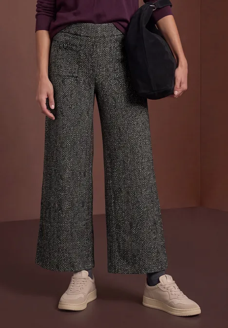 Pantalon ample gris texturé taille haute, baskets claires et sac noir porté sur l’épaule.