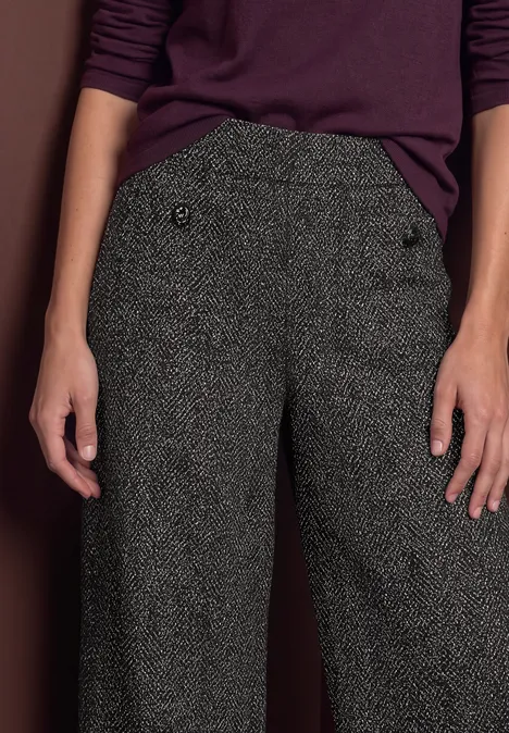 Vue de la taille aux cuisses d'une personne en pantalon ample gris à boutons et haut violet.