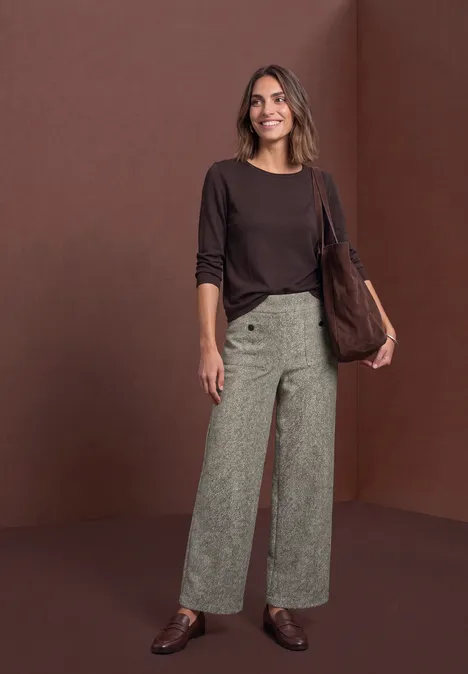 Pantalon taille haute à jambes larges, coupe décontractée bark brown Frau in braunem Oberteil, weiten gemusterten Hosen und Tasche vor braunem Hintergrund, lächelnd.