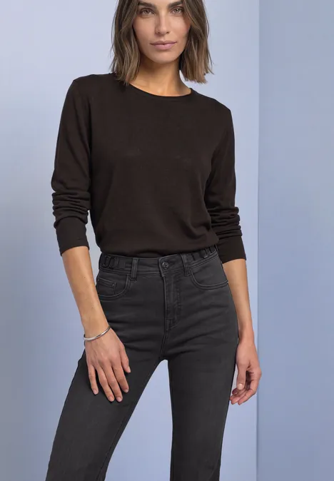 Bootcut-jeans met Mid Waist-taille in Slim Fit Black Washed Frau in braunem Langarmshirt und dunkler Jeans steht vor neutralem Hintergrund.
