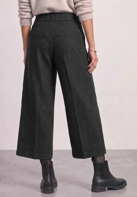Culotte met High Waist en Loose Fit-pasvorm Black Rückenansicht: Schwarze, weite, knöchellange Hose mit hellem Pullover und schwarzen Boots.