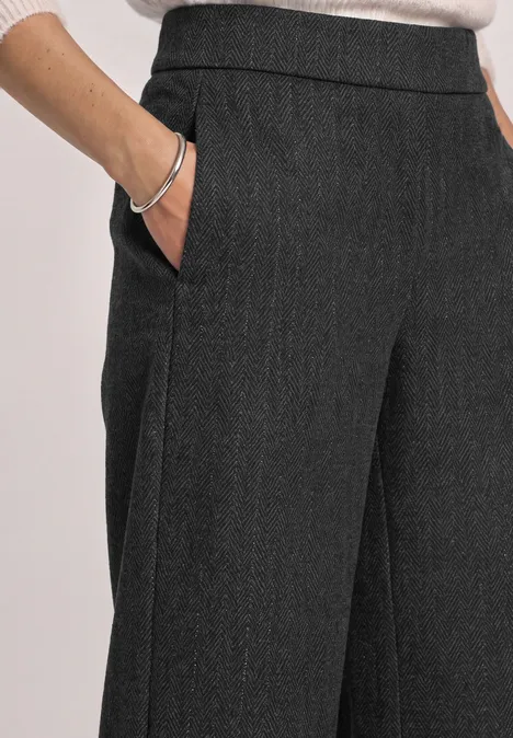 Culotte met High Waist en Loose Fit-pasvorm Black Dunkelgraue Stoffhose mit weitem Bein und Eingrifftaschen, Hand in Tasche, silbernes Armband sichtbar.