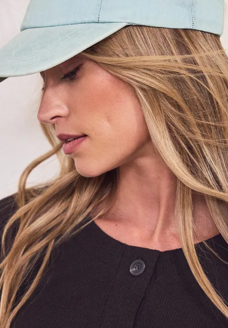 Persoon met lang blond haar, draagt lichtblauwe pet en donkere bovenkleding, gezicht onscherp.