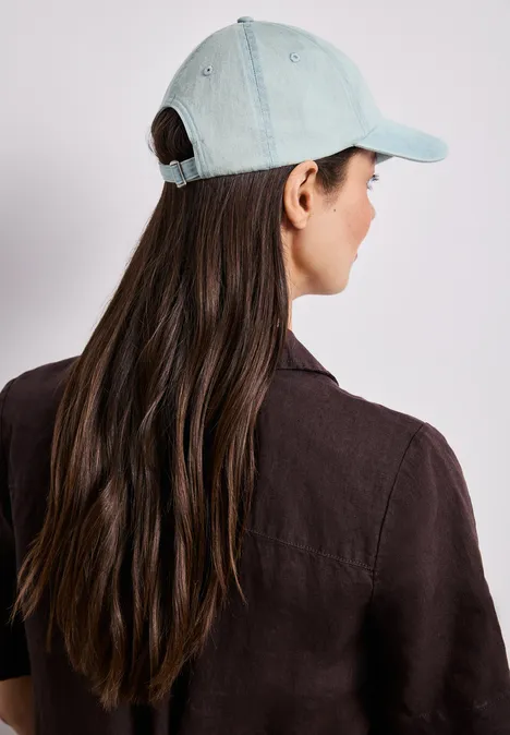 Persoon van achteren met lang, donker haar en een lichtblauwe baseballpet.