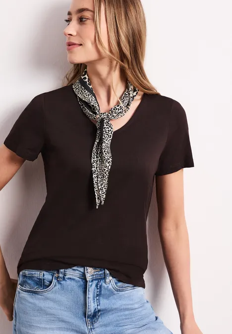 Frau mit schwarzem T-Shirt, hellblauen Jeans und gemustertem Halstuch, Gesicht verschwommen.