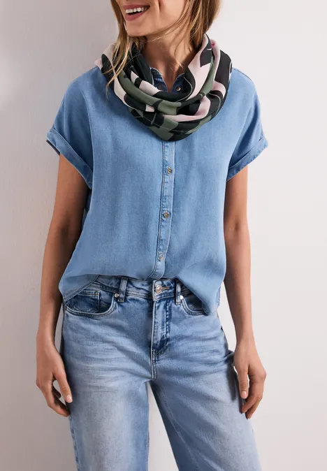 Eine Frau trägt eine helle Jeansbluse und -jeans mit buntem Schal.