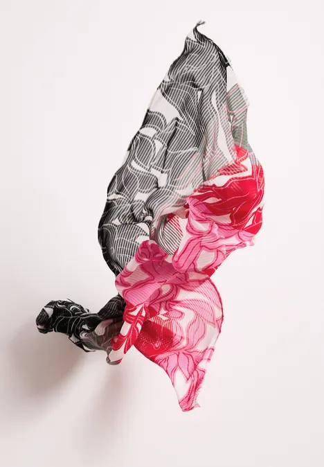 Ein schwebendes Tuch mit floralen Mustern in Schwarz, Weiß und kräftigem Rot vor weißem Hintergrund.