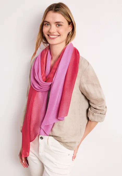 Frau trägt beige Leinenbluse und rosa-violetten Schal vor weißem Hintergrund.