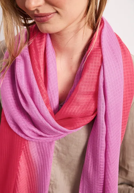 Eine Frau trägt einen rosa-rot verlaufenden Schal locker um den Hals.