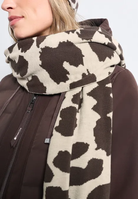 Manteau marron et écharpe à motif de taches de vache, soigneusement enroulée autour du cou.