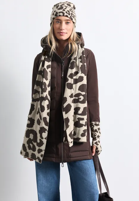 Femme en veste marron, jean bleu et ensemble beige à imprimé léopard : bonnet, écharpe et gants.
