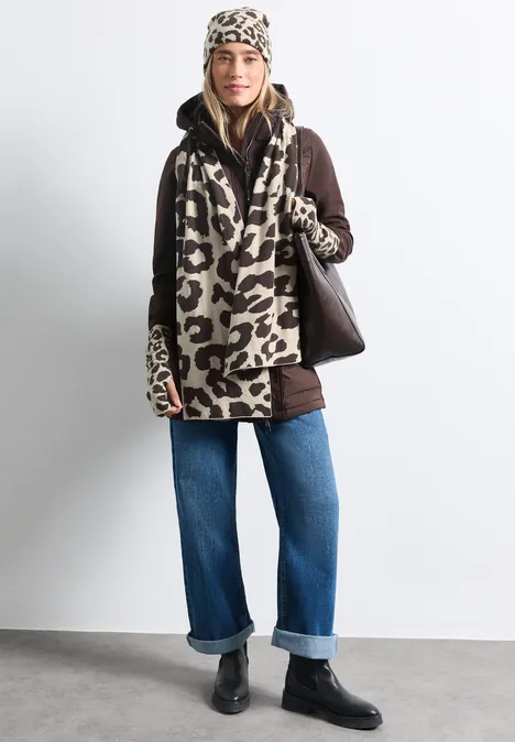 Femme en manteau léopard décontracté avec bonnet assorti, jean ample et bottines noires, tenant un grand sac.