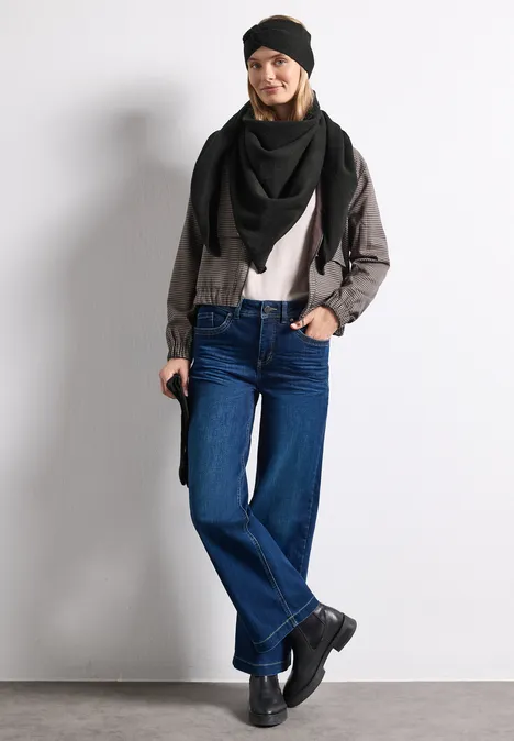 Frau in schwarzer Mütze, Dreieckstuch, grauer Jacke, weißem Shirt, weiten Jeans und schwarzen Boots.