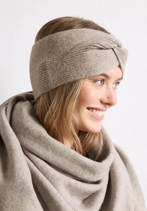 Eine lächelnde Frau mit einem beigefarbenen Strickstirnband und passendem Wollschal.