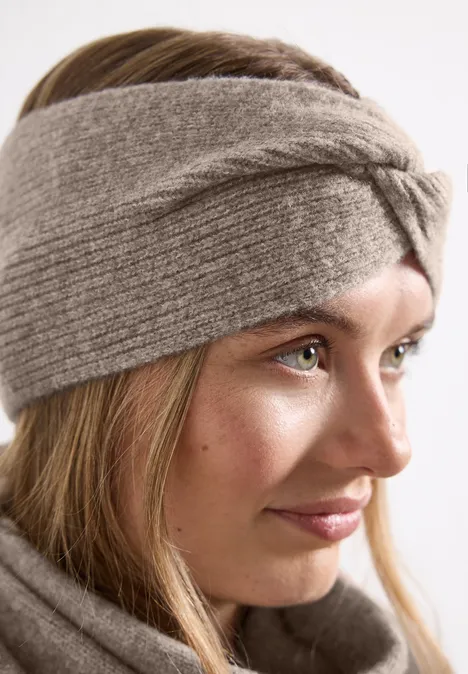 Junge Frau im Profil mit grauem, gestricktem Stirnband und passendem Schal, dezent lächelnd.