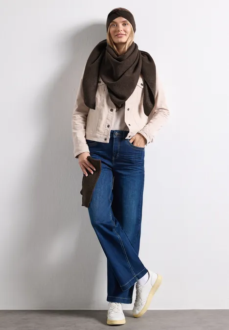 Feinstrick Stirnband in Unifarbe auburn brown mel. Stylische Person in Jeans, beiger Jacke, dunklem Schal und weißen Sneakern posiert vor weißem Hintergrund.