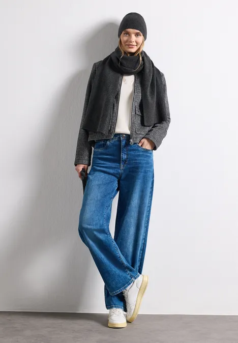 Feinstrick Beanie in Unifarbe anthracite melange Frau in weiten Jeans, weißem Shirt, schwarzer Jacke, Schal und Mütze posiert lässig vor weißem Hintergrund.