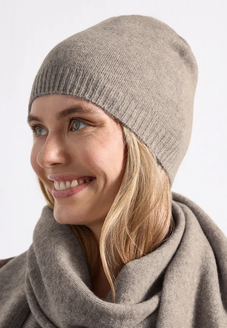 Junge Frau lächelt seitlich, trägt graubeige Strickmütze und passenden Schal.