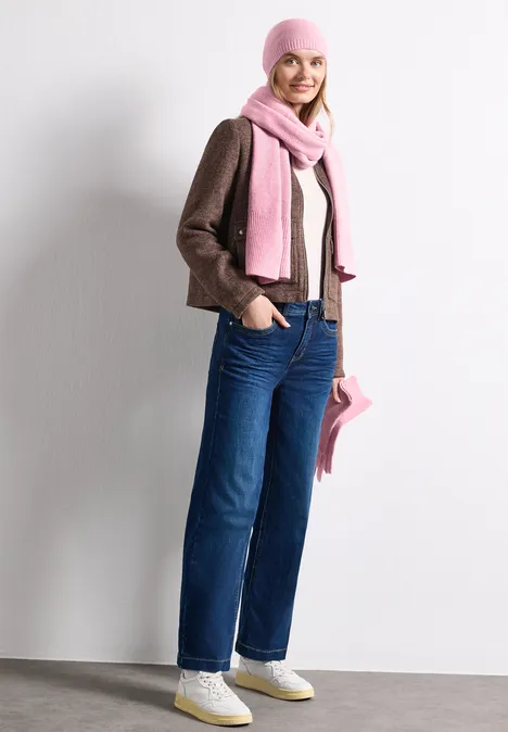 Junge Frau in Jeans, brauner Jacke und rosa Mütze mit passendem Schal und Tasche.