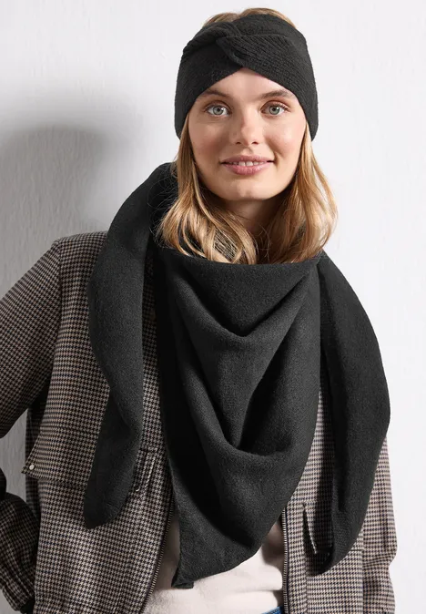 Feinstrick Dreieckstuch in Unifarbe Black Frau mit schwarzem Stirnband und Dreieckstuch in schickem Karomantel, lächelnd vor heller Wand.