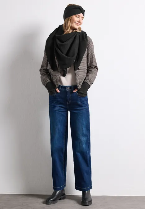 Feinstrick Dreieckstuch in Unifarbe Black Frau in Jeans, grauer Jacke, schwarzem Schal und Mütze, steht vor weißem Hintergrund, lächelnd.