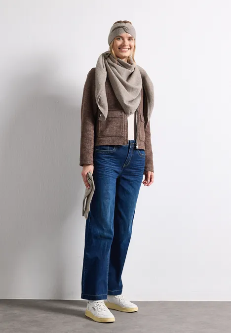 Feinstrick Dreieckstuch in Unifarbe Sandy Mocca Mel. Frau vor heller Wand, lächelt, trägt Jeans, braune Jacke, Schal, Halstuch, weiße Sneaker und Clutch.
