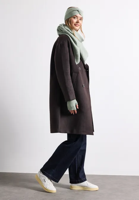 Feinstrick Dreieckstuch in Unifarbe eucalyptus green mel. Eine lächelnde Frau trägt Winterkleidung: hellgrünen Schal, Mütze, dunklen Mantel, weite Hosen und weiße Sneaker.