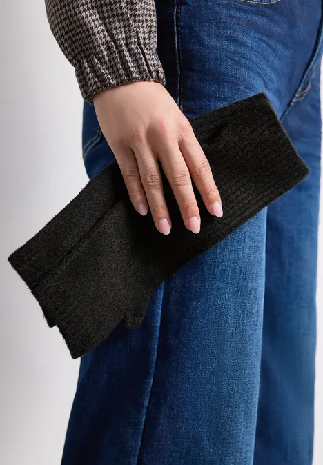 Person in Jeans und Hemd hält einen schwarzen Strickschal in der Hand.