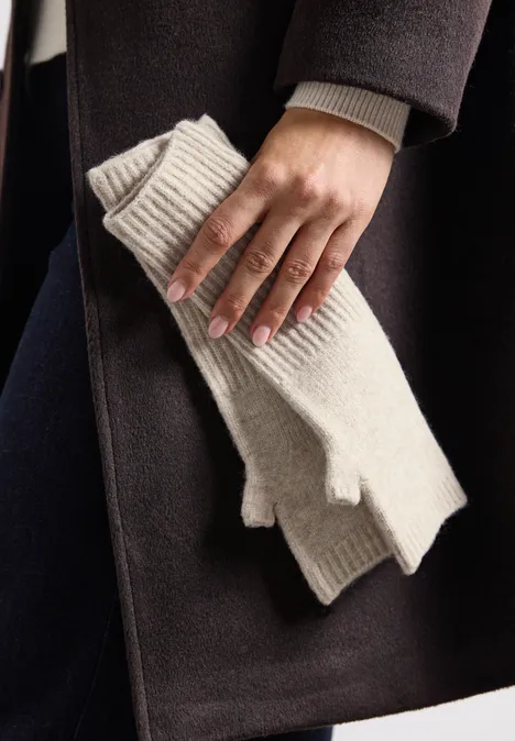 Une main tient des mitaines tricot crème devant un manteau sombre.