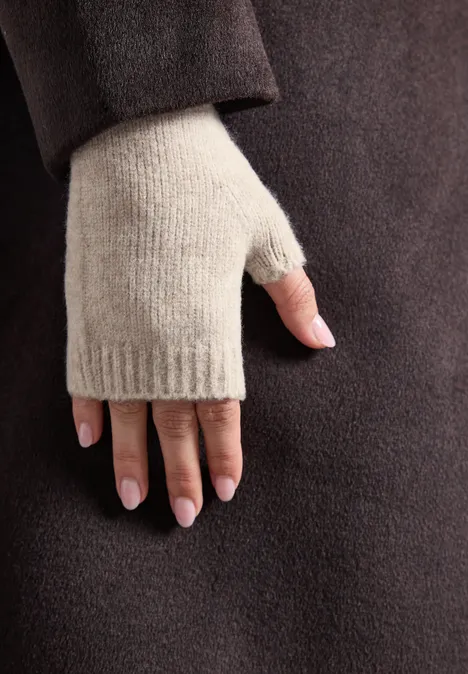 Main portant une mitaine beige devant un manteau brun foncé.