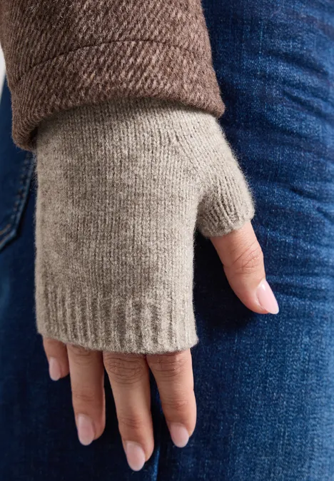 Eine Hand trägt einen grauen, fingerlosen Strickhandschuh, auf Jeans und brauner Jacke.
