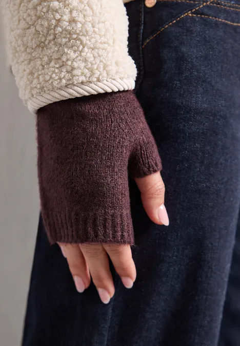 Fijn gebreide armwarmers in effen kleur rustic rouge mel. Hand met bordeauxrode gebreide vingerloze want, met beige jaszoom en donkerblauwe jeans