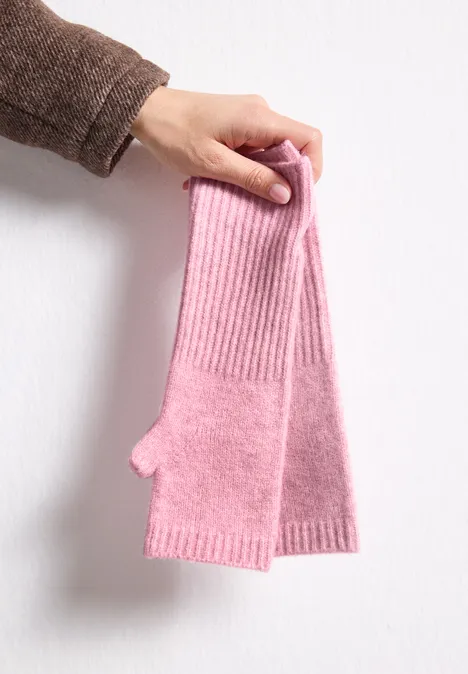 Fijngebreide armwarmers in effen kleur vintage blush mel. Een hand houdt roze, gebreide, vingerloze polswarmers vast.