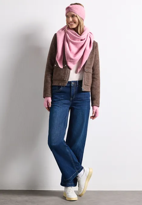 Fijngebreide armwarmers in effen kleur vintage blush mel. Vrouw in bruin jasje, roze sjaal en haarband, wijde jeans en witte sneakers voor een witte achtergrond.