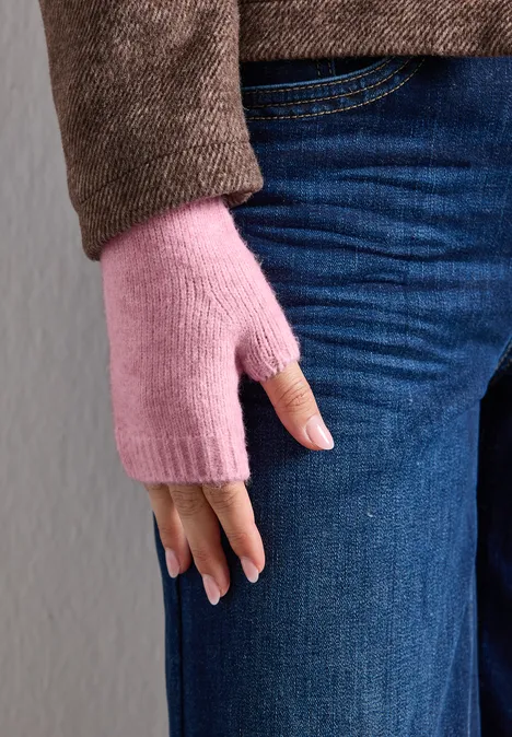 Fijngebreide armwarmers in effen kleur vintage blush mel. Close-up van persoon met blauwe spijkerbroek en bruine trui, met roze vingerloze handschoenen.