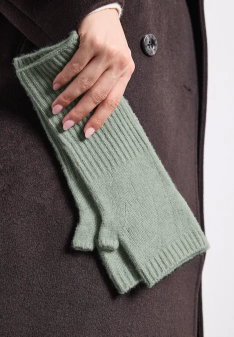 Eine Hand mit grünen, gerippten, fingerlosen Handschuhen vor einem dunklen Mantel
