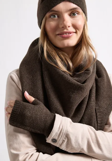 Fijngebreide armwarmers in effen kleur auburn brown mel. Een jonge vrouw draagt een bruine muts, een dikke omslagdoek en een beige shirt met duimgaten.