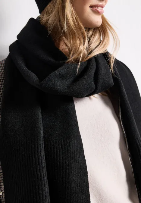 Lange, fijngebreide sjaal in effen kleur Black Een persoon draagt een zwarte wollen sjaal en zwarte muts bij een lichtbeige trui.