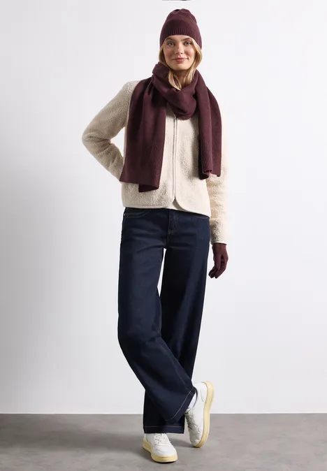 Junge Frau im Winteroutfit mit Mütze, Schal, Jacke, Jeans und Sneakern