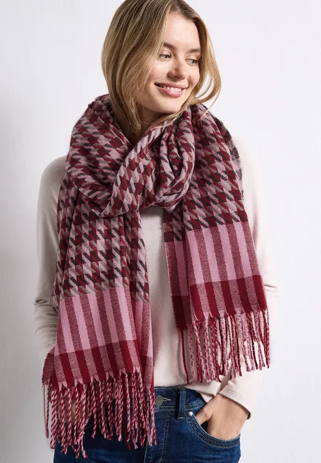 Femme souriante portant une écharpe rose et bordeaux à rayures et pied-de-poule.