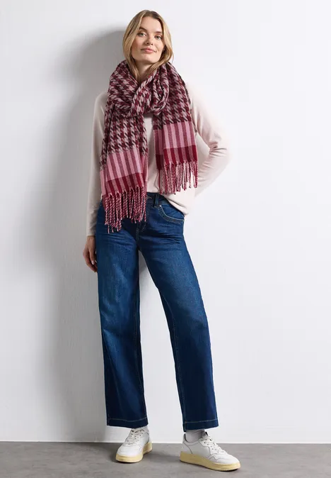 Femme portant un pull en maille clair, une écharpe à carreaux rose, un jean bleu et des baskets blanches.