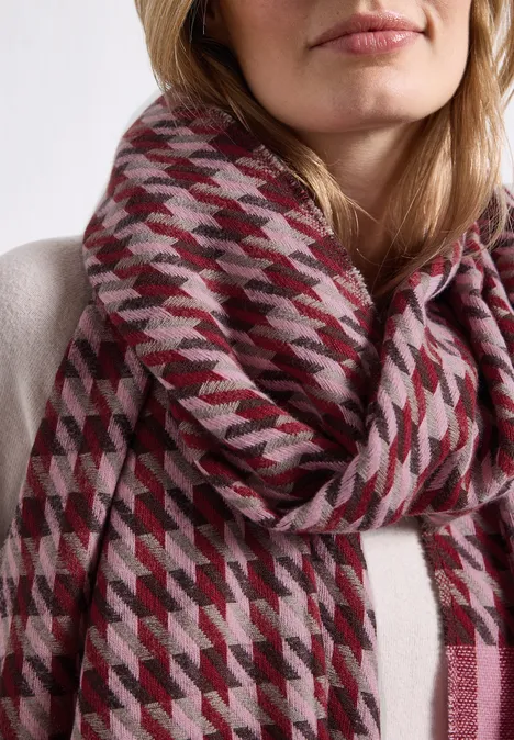 Femme portant un épais foulard à motif pied-de-poule rouge et gris sur un pull clair.