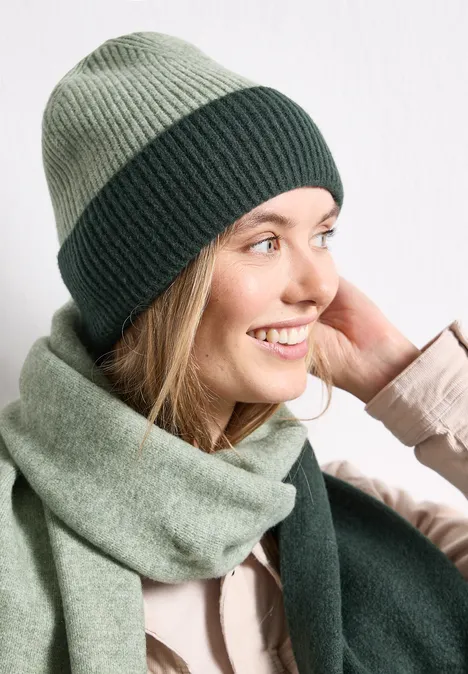 Femme portant un bonnet et une écharpe verts bicolores, souriante.