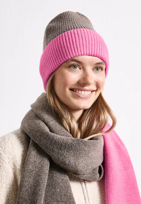 Femme souriante portant un bonnet bicolore (rose et gris) et une écharpe assortie.
