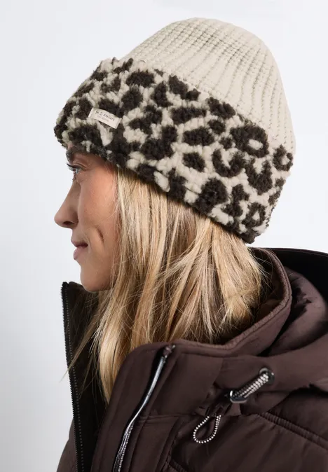 Profil d’une femme portant un bonnet beige à motif léopard et une doudoune marron.