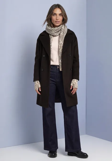 Jacquard Armwärmer mit Leo-Muster barley beige mel. Frau in dunkelbraunem Mantel, heller Strickjacke, weiter Jeanshose und beigem Schal vor hellblauem Hintergrund.