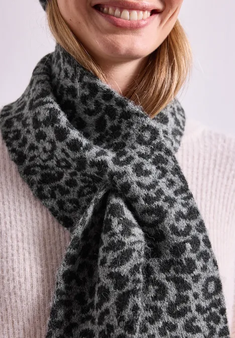 Eine Person trägt einen grauen Strickschal mit Leopardenmuster, vorne zugeknotet.