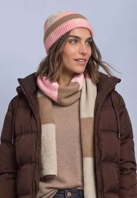 Frau trägt braune Steppjacke, beigen Pullover, rosé-beige Mütze und passenden Schal.