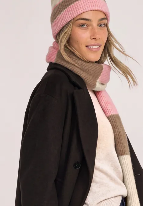 Schal mit Colorblock-Muster warm blush mel. Junge Frau in schwarzem Mantel und rosa-beigem Strickschal und Mütze lächelt leicht.
