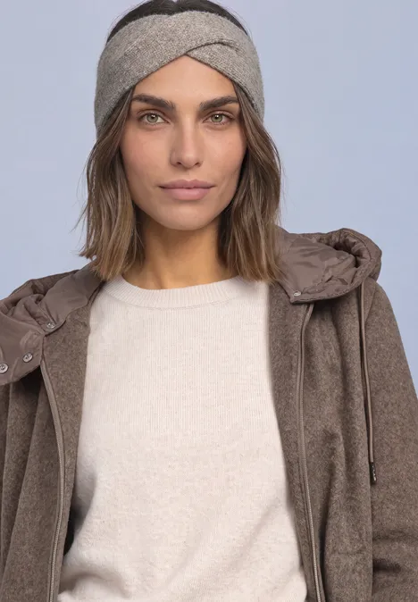 Stirnband in Melange-Optik Muddy Mocha Junge Frau mit braunem Mantel, hellem Pullover und grauem Stirnband vor neutralem Hintergrund.